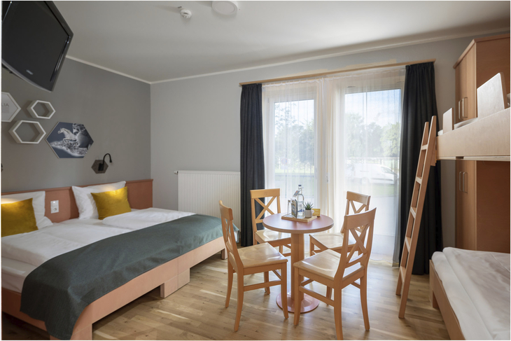 Hotelzimmer mit Doppelbett, Etagenbett und Tischgruppe im JUFA Kempten Familien-Resort