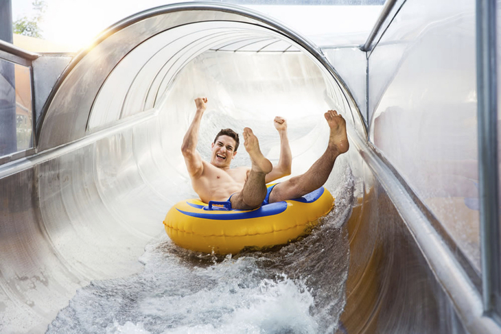 Mann rutscht in einem gelben Schlauchreifen durch eine Wasserrutsche.