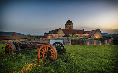 JUFA Hotel Kronach bei Abenddämmerung mit Festung Rosenberg im Sommer.