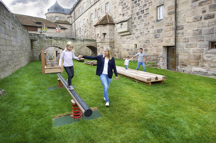Mutter und Tochter spielen auf einem Spielplatz vor historischer Kulisse.