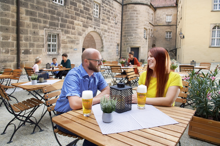 Paar sitzt an Holztisch im Innenhof eines historischen Gebäudes bei Getränken.