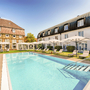 Hotelpool mit Liegestühlen und Sonnenschirmen, umgeben von Gebäuden bei sonnigem Wetter.