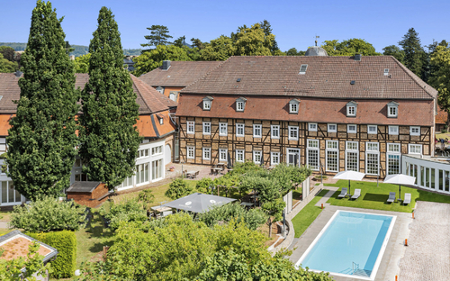 Luftaufnahme eines historischen Gebäudes mit Pool und Garten im Welcome Hotel Bad Arolsen.