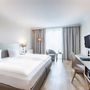 Modernes Hotelzimmer mit zwei Betten, Schreibtisch, TV und Fenster.