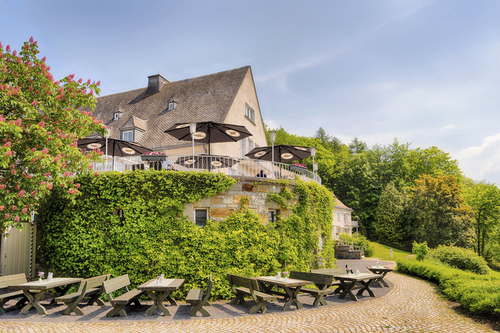 Hotelterrasse mit Sitzmöglichkeiten, von Efeu bewachsenes Gebäude, blauer Himmel.