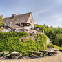 Hotelterrasse mit Sitzmöglichkeiten, von Efeu bewachsenes Gebäude, blauer Himmel.