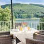 Gedeckter Tisch auf Terrasse mit Seeblick und Wald im Hintergrund.
