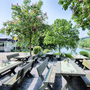 Biergarten mit Holztischen unter blühenden Bäumen am Ufer eines Sees.