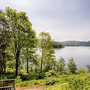 Blick auf einen See mit Bäumen und einer Bank im Vordergrund.