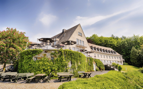 Außenansicht des Welcome Hotel Meschede mit Terrasse und grüner Umgebung.