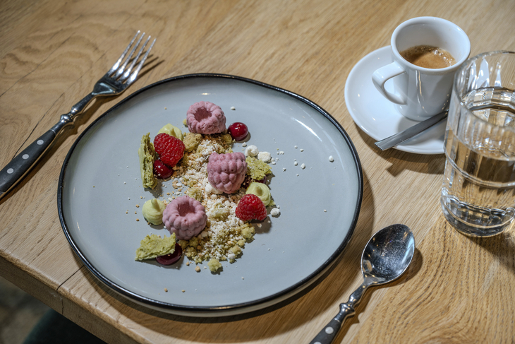 Dessert mit Himbeeren und Creme auf grauem Teller neben Espresso und Wasser.