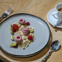 Dessert mit Himbeeren und Creme auf grauem Teller neben Espresso und Wasser.