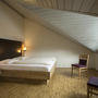 Schlafzimmer in der Ferienanlage Titisee, mit Dachschräge, Holzfußboden, Doppelbett und zwei Stühlen..