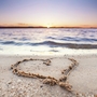Ein Herz im Sand am Strand der Ostsee bei Sonnenuntergang.