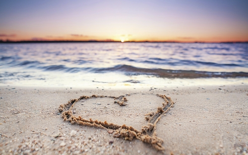 Ein Herz im Sand am Strand der Ostsee bei Sonnenuntergang.