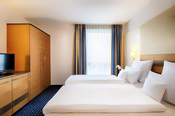 Hotelzimmer mit zwei Einzelbetten, modernem Dekor und großem Fenster.