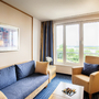 Wohnbereich einer Hotelsuite mit Sofa, Sessel und Fenster mit Blick nach draußen.