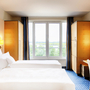 Helles Hotelzimmer mit zwei Betten, großem Fenster und Schreibtisch.