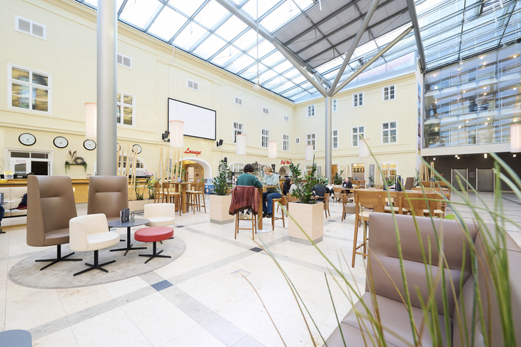 Lichterfüllter Atriumbereich mit Sitzgelegenheiten und Pflanzen im JUFA Hotel Wien City.
