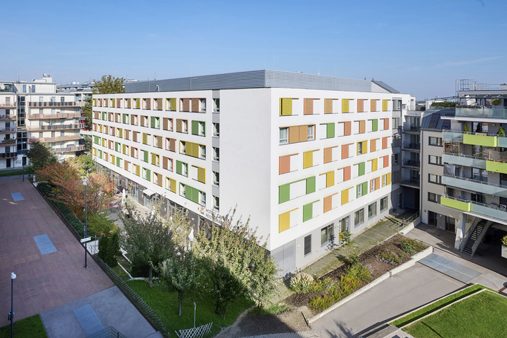 Mehrstöckiges Gebäude mit bunten Fensterläden in städtischer Umgebung.