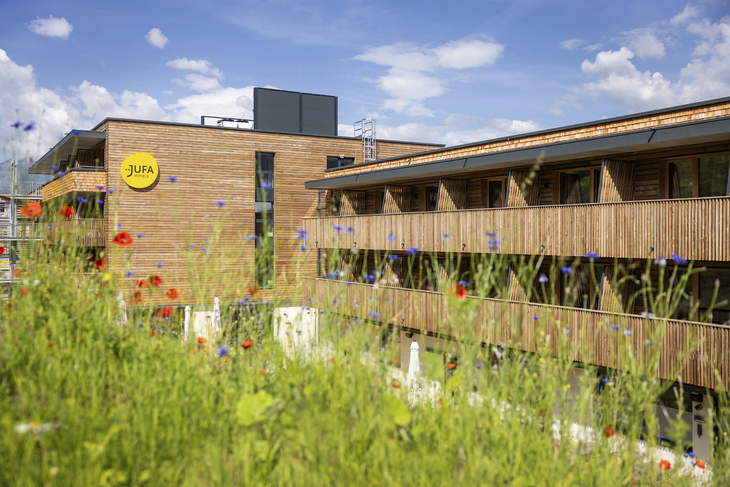 Holzgebäude des JUFA Hotels Werfenweng vor einem blühenden Garten.