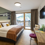 Hotelzimmer mit Doppelbett, Schreibtisch, TV und Balkonblick auf die Berge.