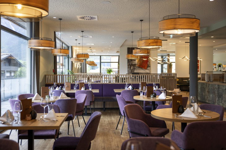 Modernes Restaurant mit gedeckten Tischen und lila Stühlen.