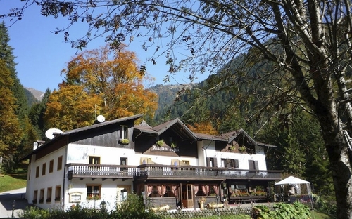 Berghütte umgeben von buntem Herbstwald und Bergen.