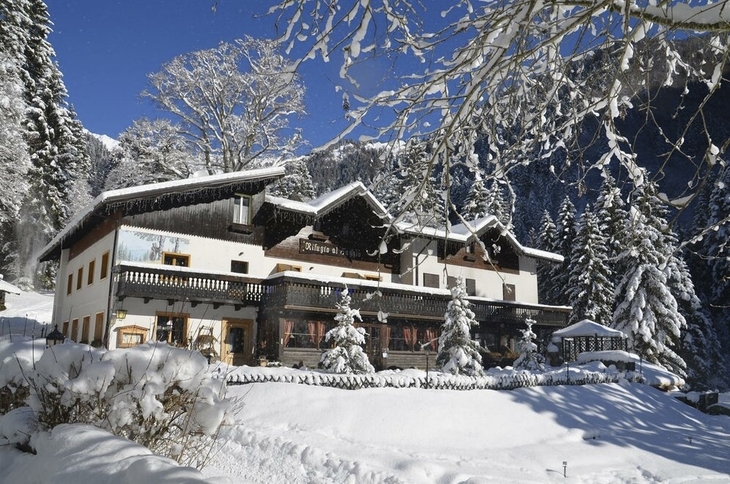 Berghütte im Winter, umgeben von verschneiten Bäumen und Bergen.