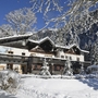 Berghütte im Winter, umgeben von verschneiten Bäumen und Bergen.