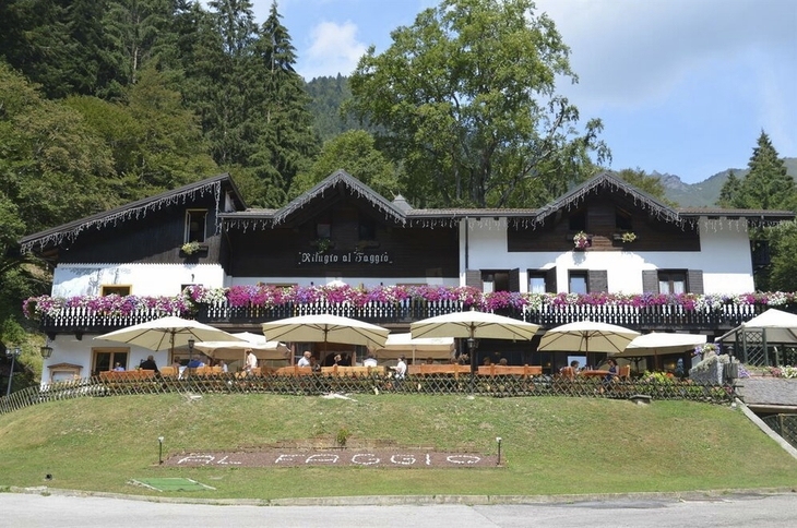 Berggasthof mit Blumen und Sonnenschirmen in grüner Landschaft.