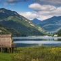 Blick auf den Ledrosee in Italien mit umliegenden Bergen und Schilf am Ufer.