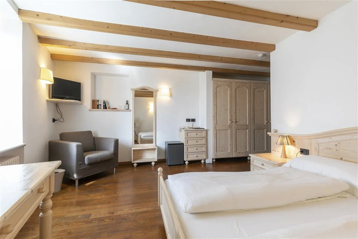 Helles Hotelzimmer mit Holzmöbeln, Doppelbett, Sessel und Spiegel.