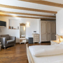 Helles Hotelzimmer mit Holzmöbeln, Doppelbett, Sessel und Spiegel.