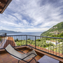 Balkon mit Liegestuhl und Blick auf See und grüne Hügel im Hintergrund