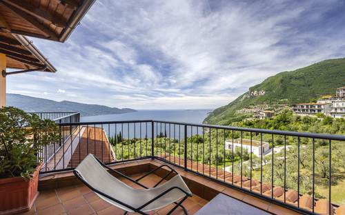 Balkon mit Liegestuhl und Blick auf See und grüne Hügel im Hintergrund