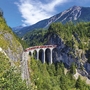 Zug auf der Landwasserviadukt-Brücke in Graubünden, umgeben von Bergen und Wald.