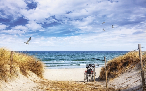 Fahrrad am Nordseestrand mit Dünen unter blauem Himmel.