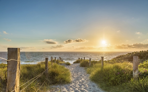 Sonnenuntergang am Strand mit Blick auf das Meer und einem sandigen Pfad.