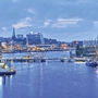 Blick auf den Hafen von Kiel bei Abenddämmerung mit beleuchteten Gebäuden und Segelschiffen.