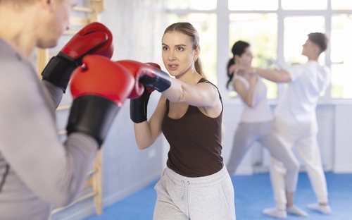 Eine Frau und ein Mann trainieren Boxverteidigung in einem Fitnessstudio.