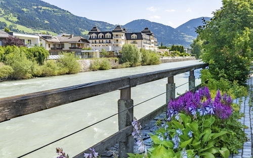 Fluss in Lienz, umgeben von Bergen und Gebäuden, mit Blumen im Vordergrund.