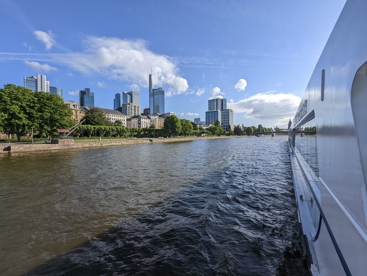 Blick vom Fluss auf Frankfurts Skyline mit Wolkenkratzern bei sonnigem Wetter.