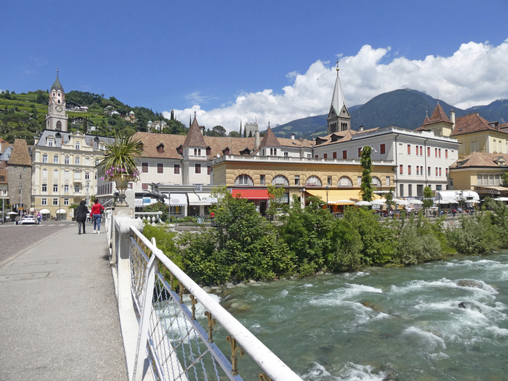 Blick auf Meran Innenstadt mit Fluss und Bergen im Hintergrund.