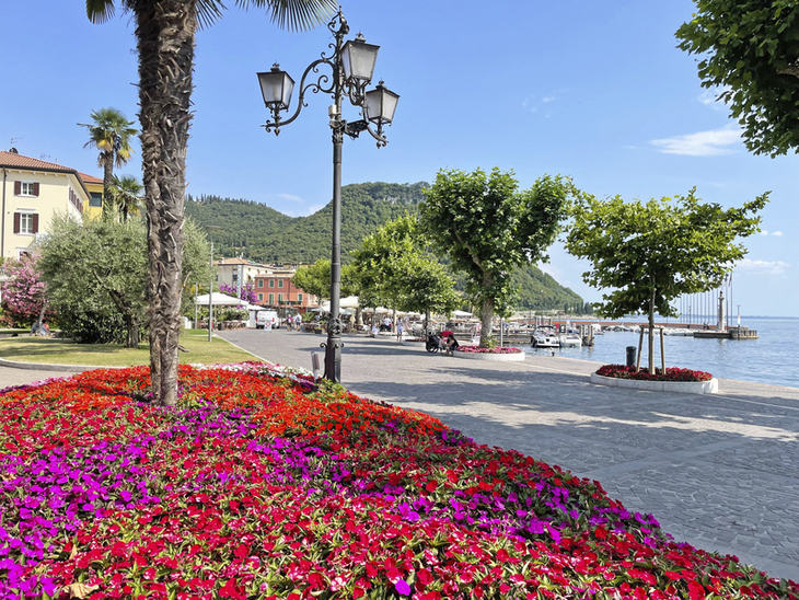 Uferpromenade am See mit bunten Blumenbeeten und Laternen.