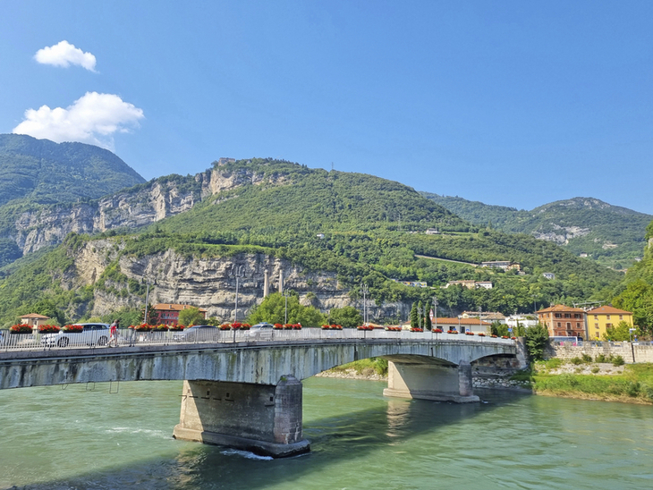 Brücke über einen Fluss mit grüner Landschaft und Bergen im Hintergrund.