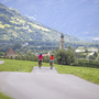 Radfahrer auf einem Weg in ländlicher Umgebung mit Kirchturm im Hintergrund.