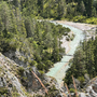 Fluss in einer alpinen Landschaft mit Brücke und Wald im Hintergrund.