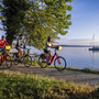 Radfahrer fahren am Starnberger See entlang, im Hintergrund Boote im Hafen.