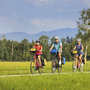 Drei Radfahrer auf einem Weg bei den Osterseen mit Bergkulisse im Hintergrund.